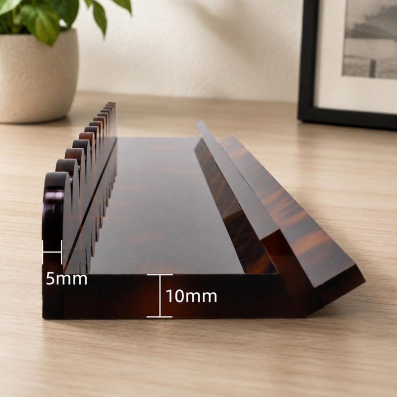 May include: A brown, tortoiseshell-patterned desk organizer with a 5mm height and 10mm depth. The organizer has a sloped design and a series of curved dividers. The product is made of a glossy material.