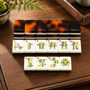 May include: A set of rectangular mahjong tiles featuring a white face with green bamboo illustrations numbered one through nine, a dragon symbol, and a dark brown tortoiseshell-patterned back. The tiles are arranged in rows on a wooden surface.