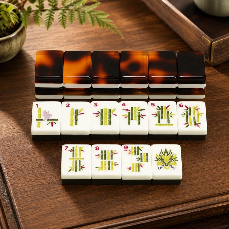 May include: A set of rectangular mahjong tiles featuring a white face with green bamboo illustrations numbered one through nine, a dragon symbol, and a dark brown tortoiseshell-patterned back. The tiles are arranged in rows on a wooden surface.