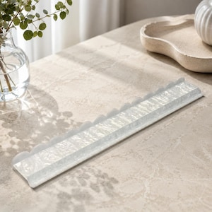 May include: A rectangular, white decorative tray with a scalloped edge. The tray has a textured, marbled appearance and is made of a glossy material. The tray is designed to hold small items and adds a touch of elegance to any space.