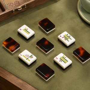 May include: A set of rectangular mahjong tiles featuring a two-toned design with a dark brown tortoiseshell pattern on one side and a white face on the other. Some tiles display green bamboo illustrations with numbers one through four in red.