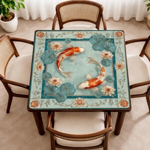 May include: Square wooden dining table featuring a koi carp and lotus flower design. The table has a light blue background with orange and white koi carp, surrounded by blue lily pads and pink lotus flowers. Four wooden chairs surround the table.
