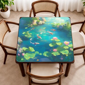 May include: Square wooden table featuring a colourful illustration of a koi pond. The image shows koi carp, lily pads, and lotus flowers in a tranquil blue water scene. The table is surrounded by four wooden chairs with woven backs and white cushions.