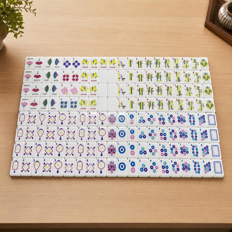 May include: A complete set of white mahjong tiles arranged in a grid, featuring colorful engraved designs including flowers, bamboo stalks, circular patterns, and seasonal symbols with numerical markings in black, blue, green, pink, and red ink.
