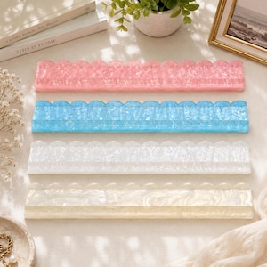 May include: Four decorative acrylic trays in pink, blue, white, and cream. Each tray has a scalloped edge design. The trays are rectangular and appear to be for organizing small items or as decorative accents.