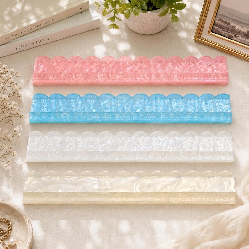 May include: Four decorative acrylic trays in pink, blue, white, and cream. Each tray has a scalloped edge design. The trays are rectangular and appear to be for organizing small items or as decorative accents.