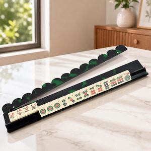 May include: A Mahjong set with black and green tile holders and ivory-colored tiles. The holders have a scalloped edge with a green marbled design. The tiles display various symbols and characters, including a "Joker" tile.