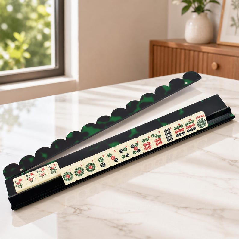 May include: A Mahjong set with black and green tile holders and ivory-colored tiles. The holders have a scalloped edge with a green marbled design. The tiles display various symbols and characters, including a "Joker" tile.
