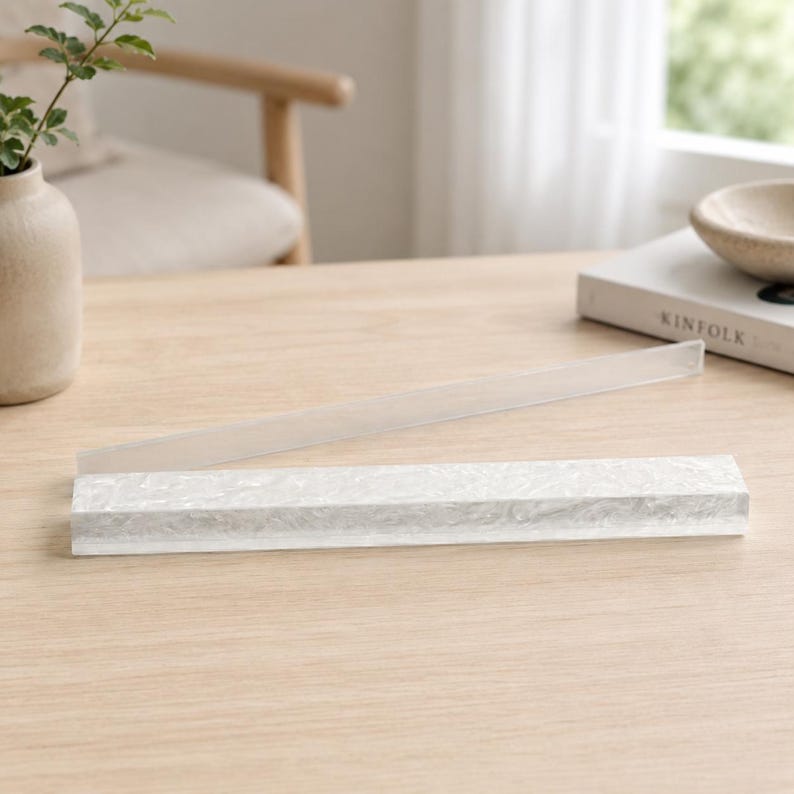May include: A rectangular, white, textured picture frame with a clear plastic cover. The frame is lying on a light-colored wooden surface. A clear plastic strip is above the frame.