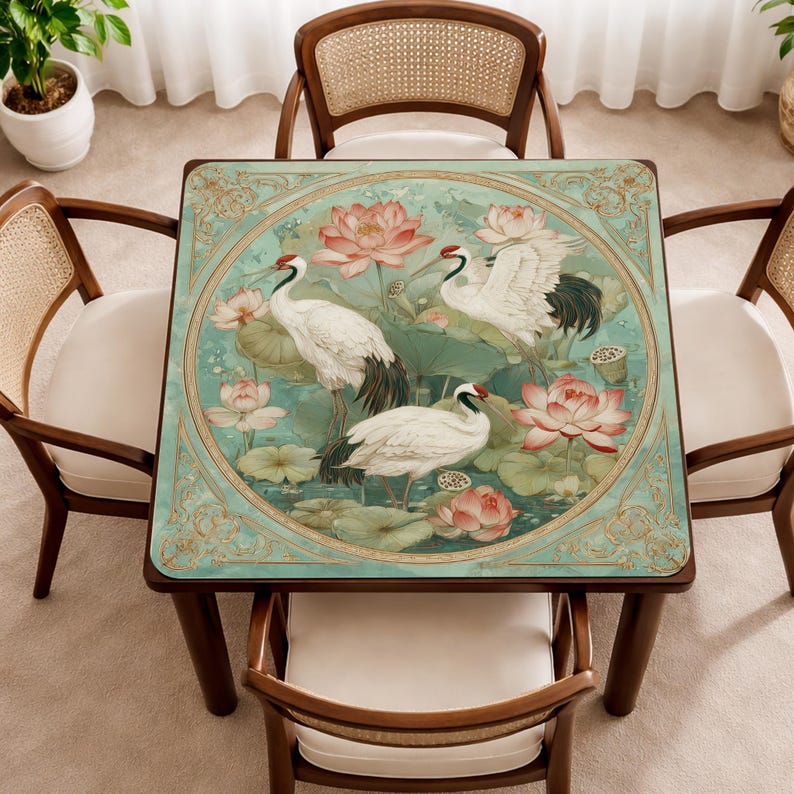May include: A square table featuring a decorative top with a circular illustration of three white cranes with black tail feathers and red crowns, surrounded by pink lotus flowers and green lily pads on a teal background with gold filigree borders.