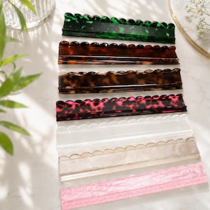 May include: A collection of decorative acrylic trays in various colors and patterns. The trays feature a scalloped edge design and include shades of green, brown, pink, and clear. The trays are ideal for organizing small items or as decorative accents.