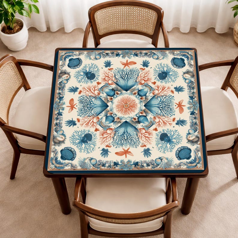 May include: A square wooden table with a marine-themed design, surrounded by four wooden chairs with woven backs and white cushions. The table's surface features a cream background with blue and coral illustrations of coral, starfish, and other sea life.