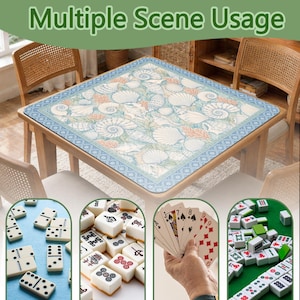 May include: A square game table mat featuring a light blue and white seashell pattern with a decorative border. The mat is displayed on a wooden table, with smaller circular insets showing dominoes, mahjong tiles, and playing cards in use.