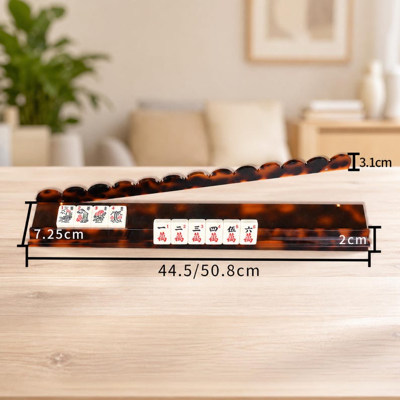 May include: A tortoise-shell patterned Mahjong tile rack with a matching tile holder. The rack is 17.5 inches long, 2.8 inches wide, and 1.2 inches tall. The holder contains white tiles with red and black symbols. The rack is on a wooden table.