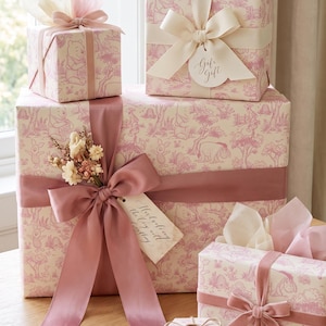 May include: Five gift boxes wrapped in cream paper with a pink toile pattern featuring Winnie the Pooh characters. The boxes are adorned with satin ribbons in shades of pink and cream, dried flower sprigs, and paper gift tags with handwritten text.