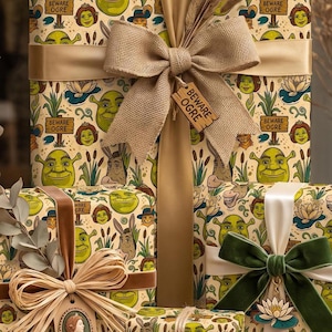 May include: Gift boxes wrapped in cream-colored paper featuring a repeating pattern of Shrek characters, swamp plants, and signs reading BEWARE OGRE. The packages are decorated with various ribbons, including burlap and velvet, and dried grass.