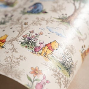 May include: A roll of wallpaper featuring a repeating pattern of Winnie the Pooh, Piglet, and Eeyore in a forest setting. The design includes delicate line drawings of trees and flowers with soft watercolor accents in yellow, pink, and blue.
