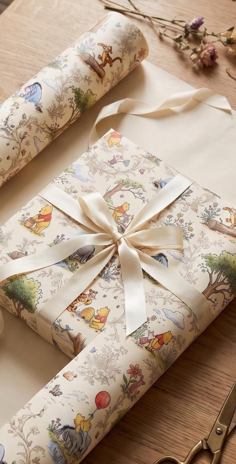 May include: A square gift box wrapped in cream-colored paper featuring a repeating pattern of Winnie the Pooh characters, trees, and flowers. The package is tied with a smooth, cream-colored satin ribbon tied in a bow at the center.