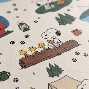 以下が含まれることがあります： キャンプをするスヌーピーとウッドストックの繰り返し模様が描かれたクリーム色の紙。イラストには、ウッドストックと一緒に丸太に座るスヌーピー、テント、松の木、ランタン、キャンプファイヤー、マグカップ、小さな黒い足跡が含まれています。