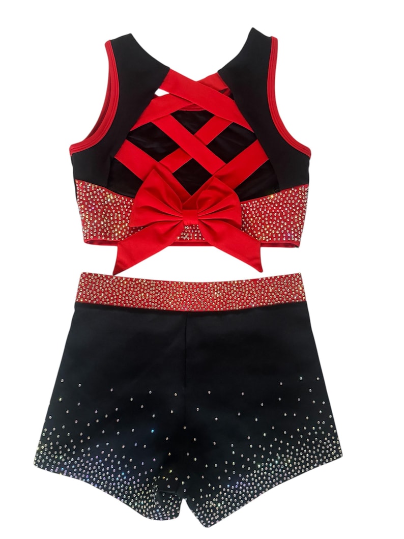 Peut inclure: Ensemble d'uniforme de cheerleading noir et rouge. Le haut pr&eacute;sente un design crois&eacute; dans le dos avec un n&oelig;ud rouge. Le haut et le short sont orn&eacute;s de strass. Le short est noir avec un d&eacute;grad&eacute; de strass.