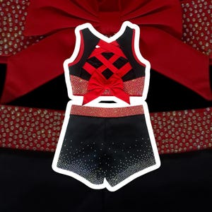 Peut inclure: Ensemble uniforme de cheerleading noir et rouge. Le haut pr&eacute;sente un dos crois&eacute; et un n&oelig;ud rouge. Le short est noir avec des strass. Le haut et le short ont une bordure rouge. Le fond est noir avec un n&oelig;ud rouge.
