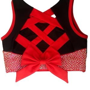 Peut inclure: Un haut court noir et rouge avec un n&oelig;ud. Le haut pr&eacute;sente un n&oelig;ud rouge &agrave; la taille et un motif crois&eacute; dans le dos. La ceinture est orn&eacute;e de strass.
