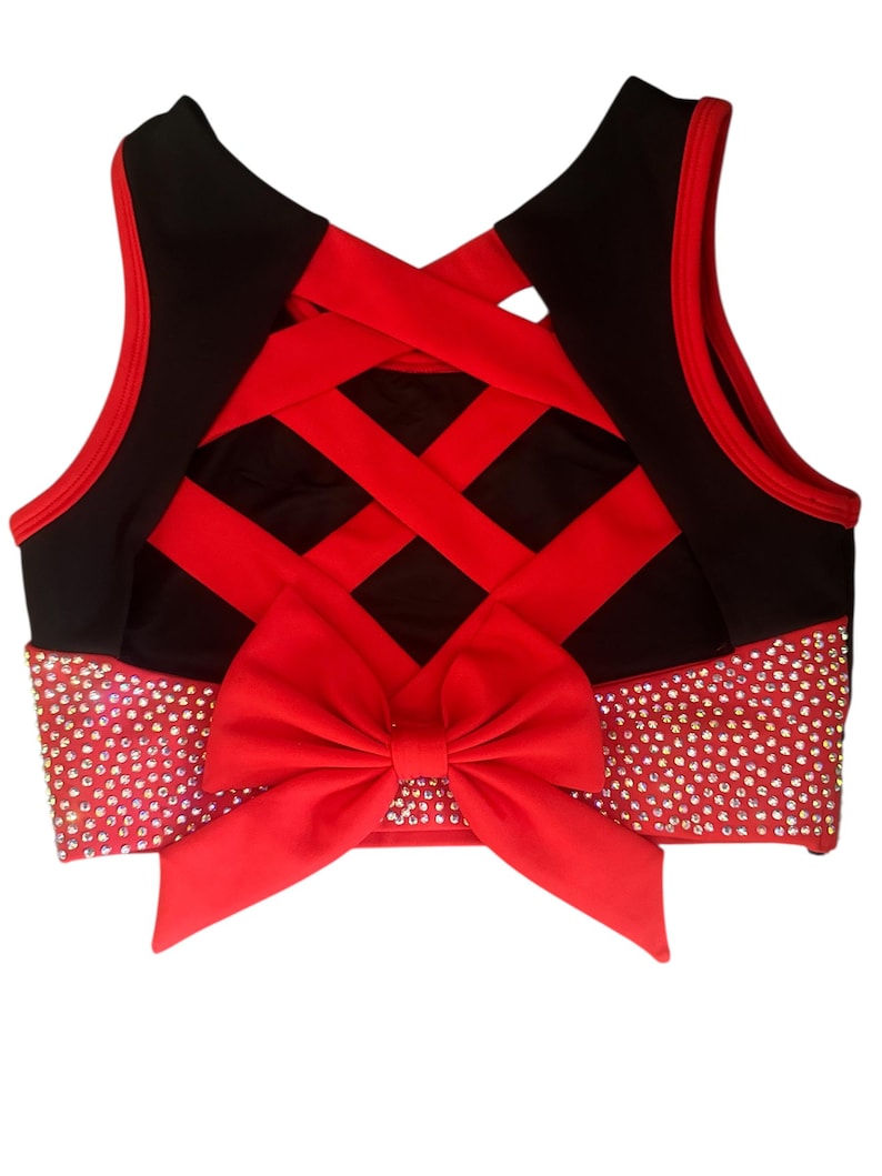 Peut inclure: Un haut court noir et rouge avec un n&oelig;ud. Le haut pr&eacute;sente un n&oelig;ud rouge &agrave; la taille et un motif crois&eacute; dans le dos. La ceinture est orn&eacute;e de strass.