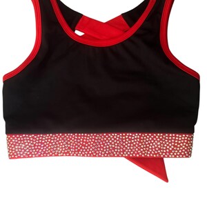 Peut inclure: Soutien-gorge de sport noir avec bordure rouge et dos crois&eacute; rouge. La bande inf&eacute;rieure est rouge et orn&eacute;e de strass &eacute;tincelants. Un morceau de tissu rouge pend du bas.