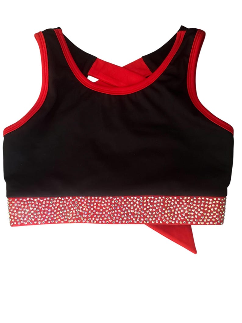 Peut inclure: Soutien-gorge de sport noir avec bordure rouge et dos crois&eacute; rouge. La bande inf&eacute;rieure est rouge et orn&eacute;e de strass &eacute;tincelants. Un morceau de tissu rouge pend du bas.