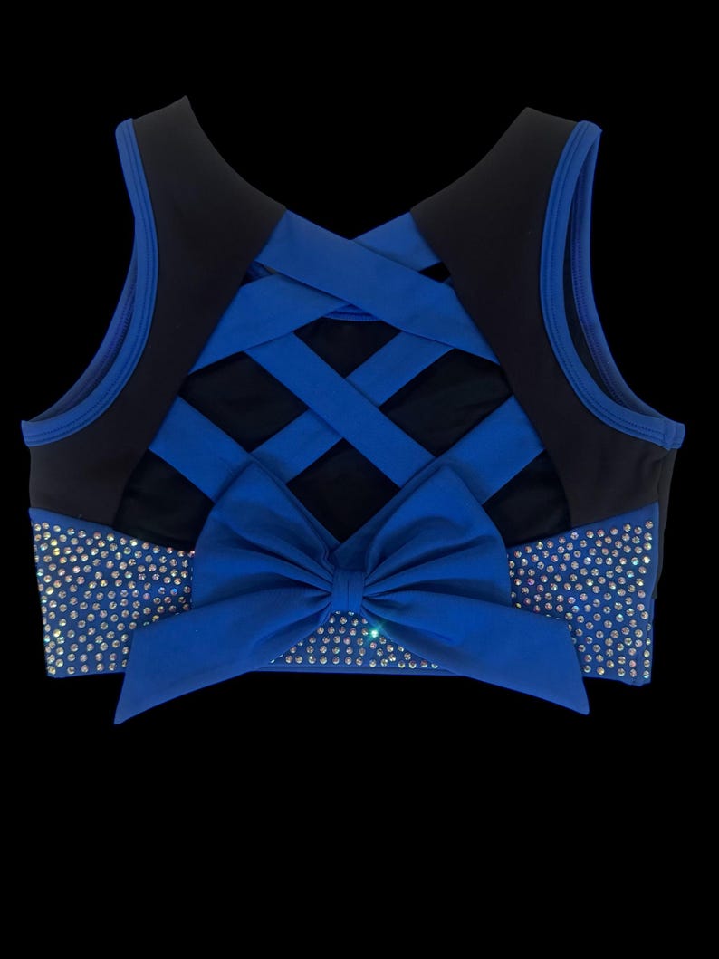 Peut inclure: Haut de sport bleu et noir avec un n&oelig;ud et des strass. Le haut pr&eacute;sente un motif crois&eacute; dans le dos et un n&oelig;ud &agrave; l'avant. Des strass sont plac&eacute;s &agrave; l'avant et sur les c&ocirc;t&eacute;s du haut.