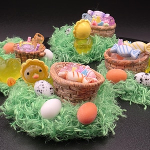 May include: An Easter-themed display featuring miniature baskets filled with colorful candies and decorative eggs. The scene includes small, yellow chick and duck figurines nestled in green, fluffy grass, creating a festive and cheerful arrangement.