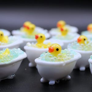 May include: A collection of miniature white bathtubs, each with a yellow rubber ducky inside. The ducks have orange beaks and black eyes, surrounded by blue and yellow bubbles. The bathtubs have small feet.