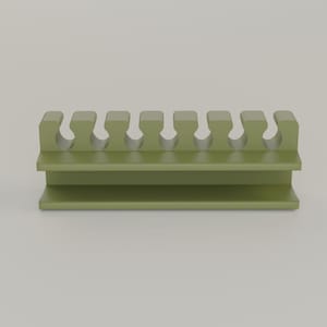 May include: A sage green, plastic object with a rectangular base and a top section featuring seven U-shaped cutouts. The object appears to be a holder or organizer, possibly for small items or tools. The design is simple and functional.