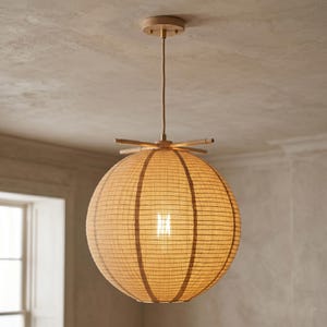 Könnte beinhalten: Eine kugelförmige Pendelleuchte mit einem gewebten, beigefarbenen Schirm und Holzakzenten. Das Licht hängt an einer Deckenhalterung aus Holz und verfügt über eine sichtbare Glühbirne. Der Schirm hat einen Durchmesser von etwa 46 cm.