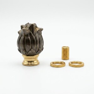 May include: A dark metallic finial shaped like a closed flower bud, featuring a polished brass base. The set includes a small threaded brass cylinder and two matching brass rings with a textured, ridged edge for secure assembly and attachment.