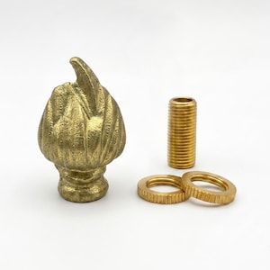 May include: A brass finial with a textured, flame-like shape, accompanied by a threaded metal pipe nipple and two matching circular knurled nuts. The components feature a metallic gold finish and are designed for assembly as a decorative hardware piece.