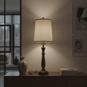 Puede incluir: Una lámpara de mesa de madera con una pantalla plisada. La lámpara tiene una base de color marrón oscuro y una pantalla de color crema. La lámpara está sobre un mueble de madera, con un jarrón y libros cerca. La habitación tiene una paleta de colores neutros.