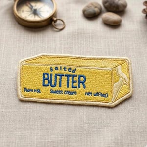 May include: Embroidered patch in the shape of a butter stick, with the word "BUTTER" in blue, and the words "salted" and "sweet cream" above and below. The patch is yellow with a white border.