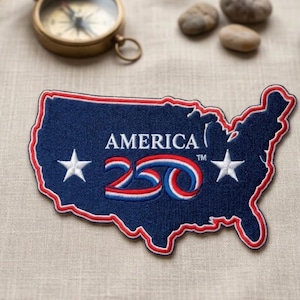 May include: A navy blue embroidered patch in the shape of the United States. The patch features the word "AMERICA" above the number "250" in red, white, and blue. Two white stars are on either side of the number. The patch is outlined in red.