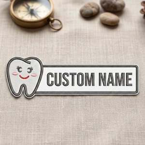 May include: A white rectangular patch with the text "CUSTOM NAME" in black. A cartoon tooth with a smiling face is on the left side. The patch has a gray border and is on a beige fabric surface.