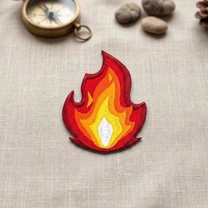 May include: Embroidered patch in the shape of a flame, featuring shades of red, orange, yellow, and white. The patch is designed with detailed stitching, creating a textured appearance. Ideal for adding to clothing or accessories.