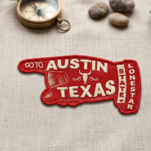 May include: A red and white embroidered patch with the words "GO TO AUSTIN TEXAS" and "LONESTAR STATE" in a unique design. The patch features a longhorn skull and a vintage illustration.