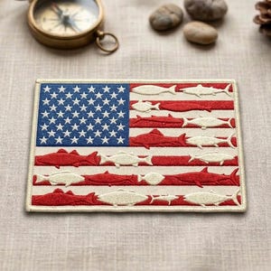May include: A rectangular embroidered patch featuring a stylized American flag design. The blue canton contains white stars, while the red and white stripes are composed of various fish silhouettes in alternating red and off-white thread colors.