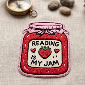 May include: Embroidered patch in the shape of a jam jar with the text "Reading is My Jam". The patch is red with a pink lid and features a strawberry and hearts.