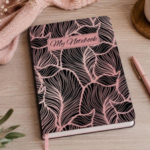 May include: A rectangular notebook featuring a black cover with a repeating pink line-art leaf pattern. A pink rectangular label on the front cover contains the text My Notebook in a black script font. A pink ribbon bookmark extends from the bottom.