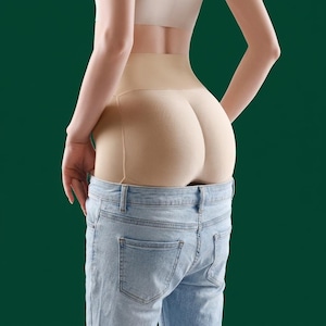 May include: Beige butt-lifting shapewear worn under light blue denim jeans. The shapewear is designed to enhance the wearer's figure. The background is a solid dark green.