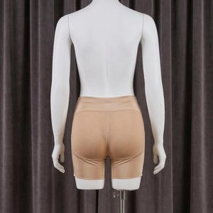 May include: Tan-colored shorts with a textured, breathable panel on the rear, displayed on a mannequin. The shorts have a smooth, solid color on the front and sides. The mannequin is white and stands against a neutral-toned backdrop.