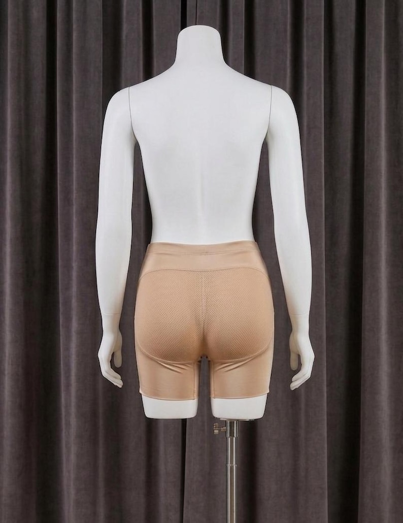 May include: Tan-colored shorts with a textured, breathable panel on the rear, displayed on a mannequin. The shorts have a smooth, solid color on the front and sides. The mannequin is white and stands against a neutral-toned backdrop.