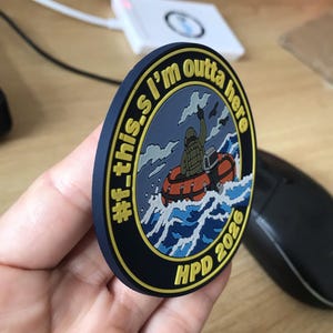 May include: A circular morale patch with a dark blue border and yellow text reading #f_this.I'm outta here and HPD 2026. The center features a graphic of a person in a life vest riding an orange inflatable boat through blue ocean waves.