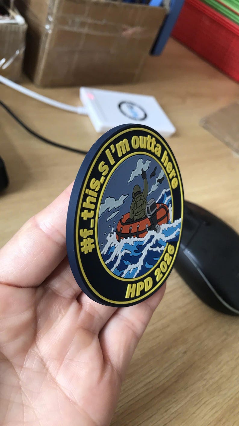 May include: A circular morale patch with a dark blue border and yellow text reading #f_this.I'm outta here and HPD 2026. The center features a graphic of a person in a life vest riding an orange inflatable boat through blue ocean waves.